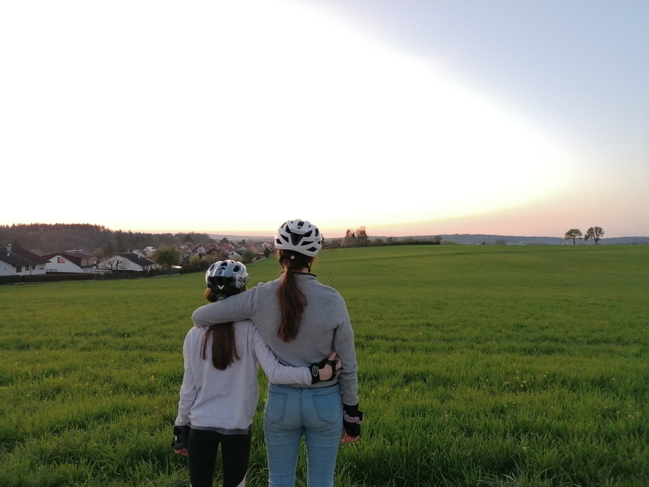 Geschwister blicken gemeinsam über ein Feld in die Abendsonne